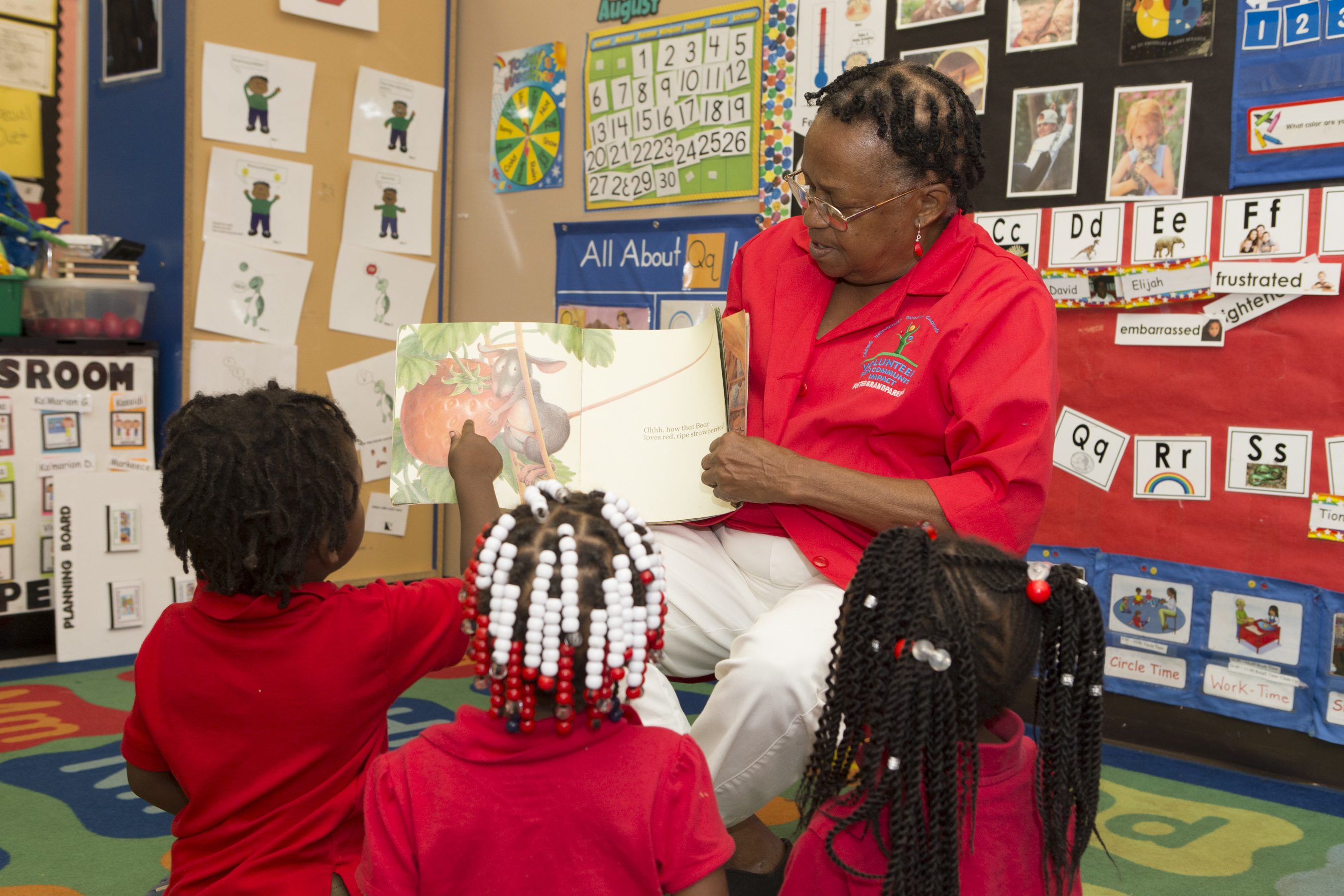 A woman is reading a picture book to young children sitting on the floor of a classroom.